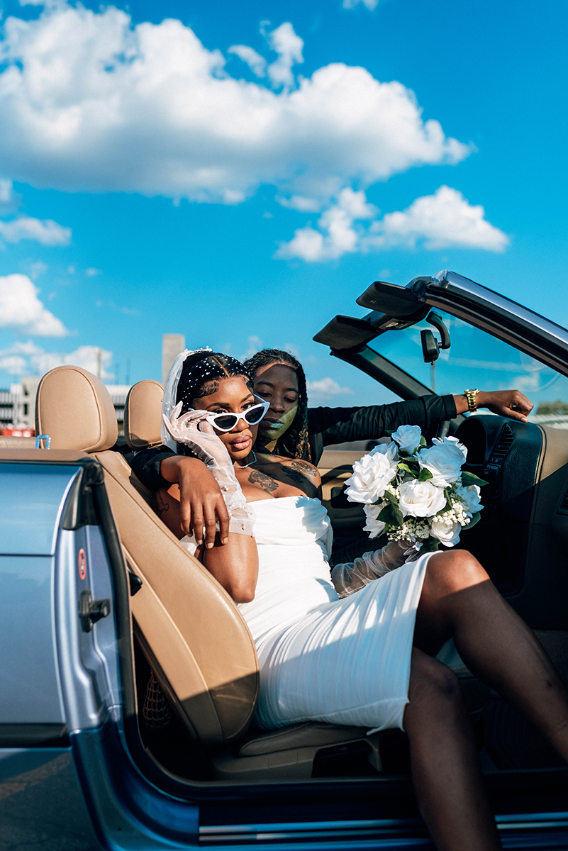 Elopement styled shoot in Camp North End Charlotte, NC with same-sex couple in classic BMW convertible. couple in front seat, bride looking at camera holding bouquet
