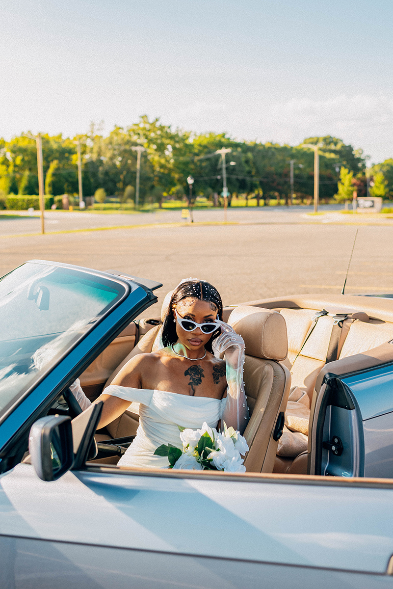 Elopement styled shoot in Camp North End Charlotte, NC with same-sex couple in classic BMW convertible. Bride in drivers seat with door open holding sunglasses