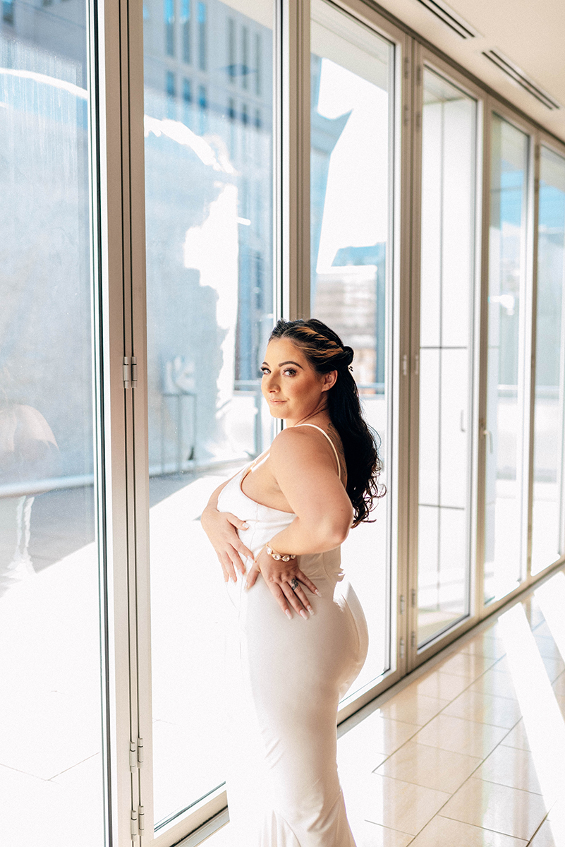 Wedding styled shoot at 220 North Tryon in Charlotte, NC and Foundation of the Carolinas art gallery. one bride standing near floor to ceiling windows posing while facing backwards
