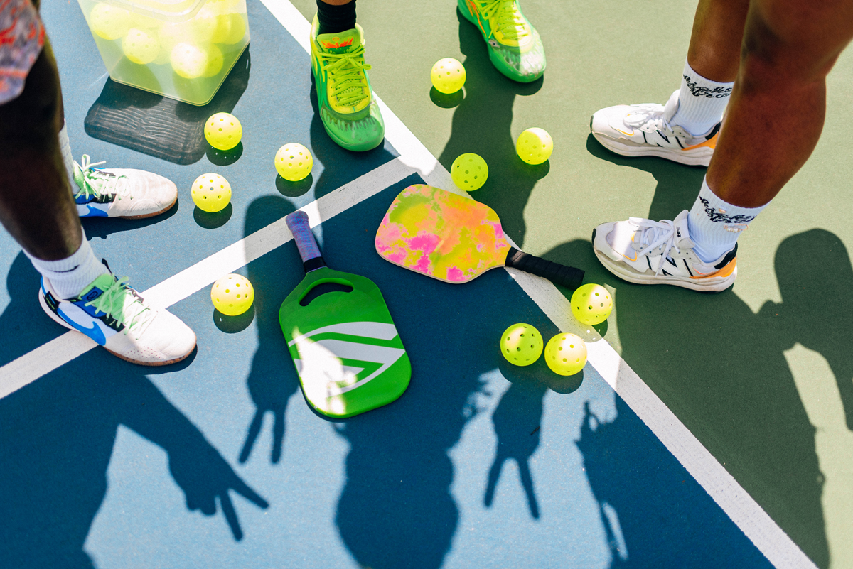 Group of people on pickleball court shoes in frame. Pickleballs surrounding paddle, shadows shown on court for BPC photoshoot