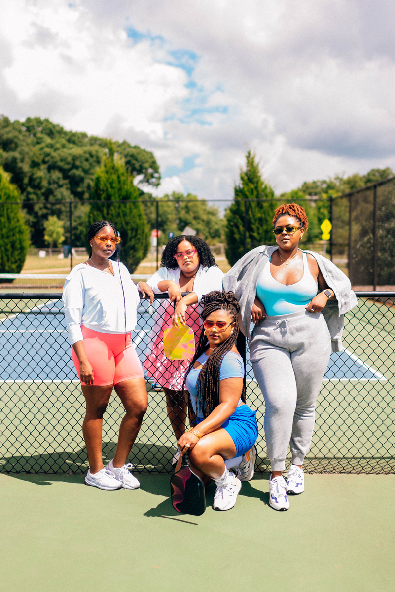 Group of women sitting in front of pickleball net dressed in 90s attire and bold colors for BPC photoshoot