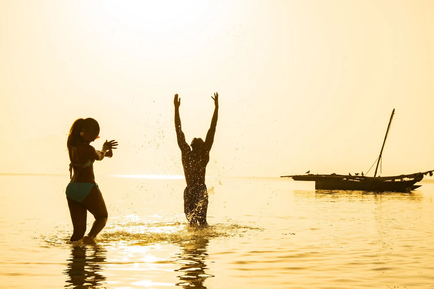 Guests playing in the ocean at sunset with a dhow on the horizon
