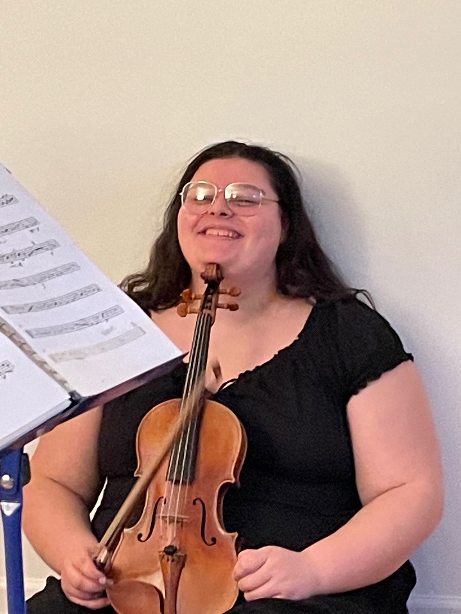Georgia sitting with her head resting on her violin, smiling.
