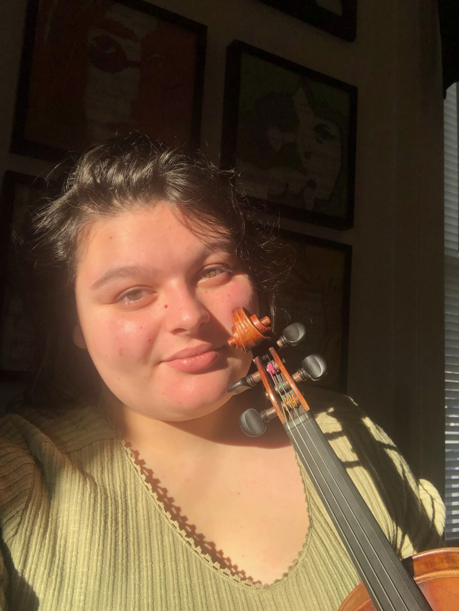 Georgia in a green sweater and her violin with the sun on her face.