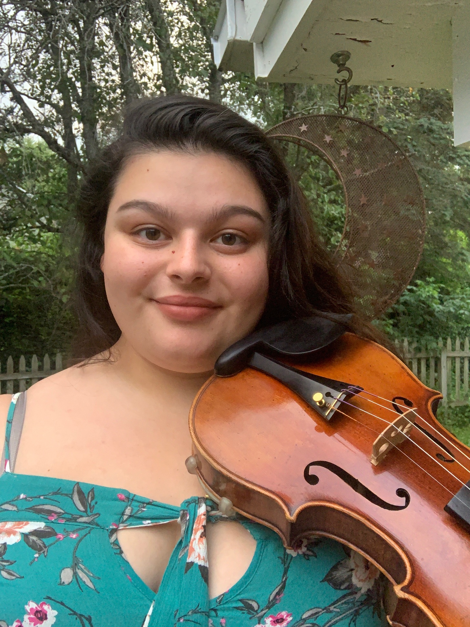 Georgia in a blue dress with her violin outside.