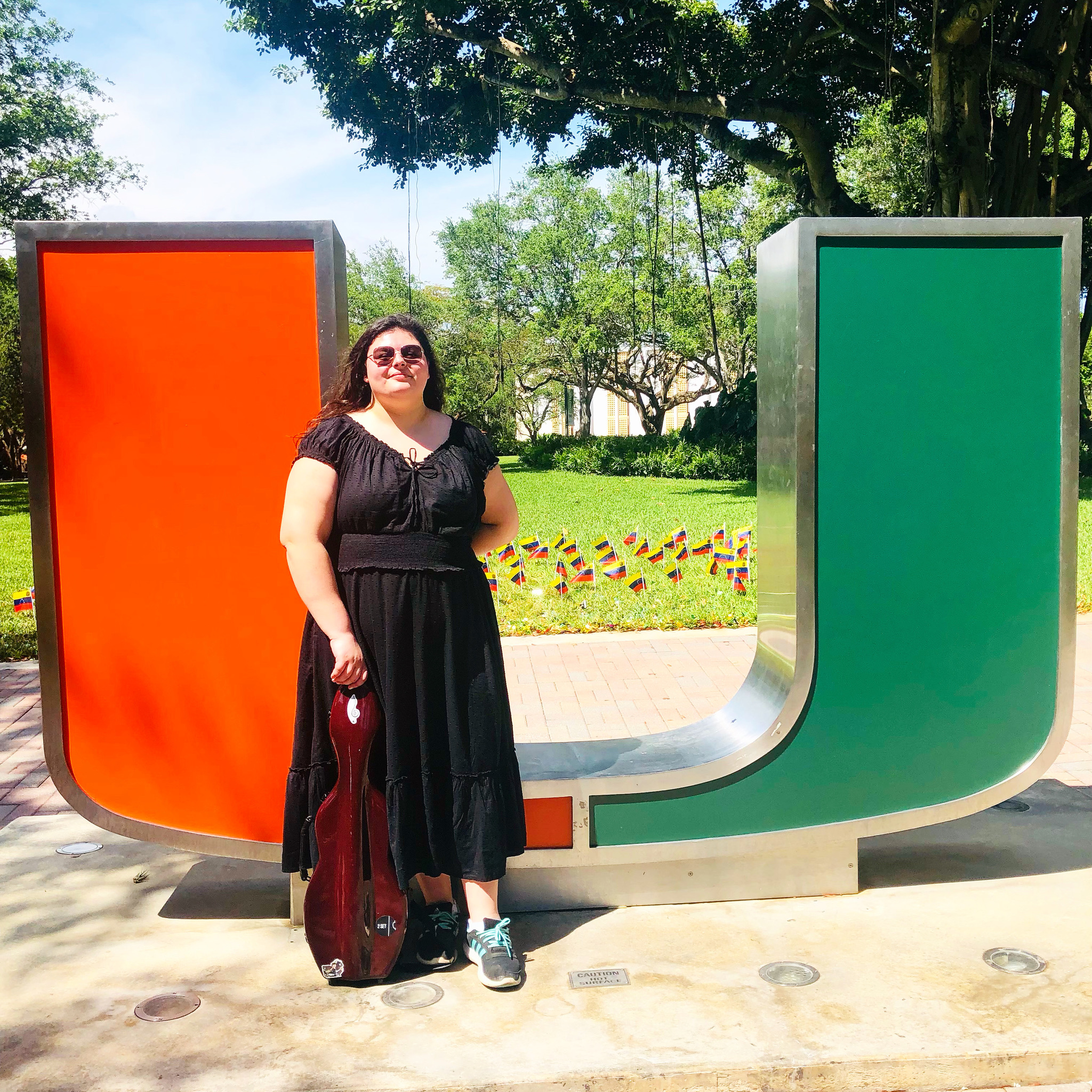 Georgia standing in front of "The Rock" (U-Miami statue) with her violin case in a black dress.