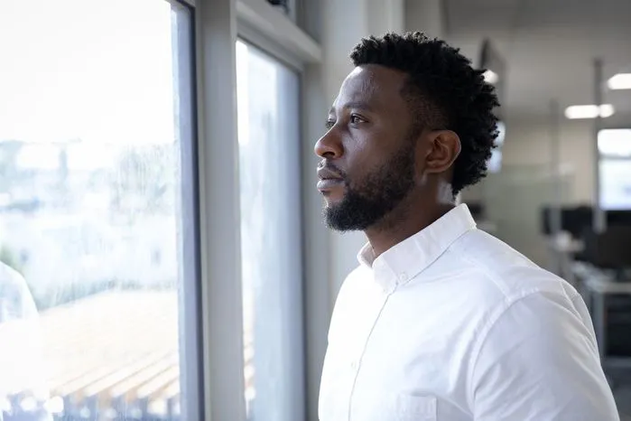 An image of a man in deep thought looking out a window in an office—discover what pessimism really means with clear definitions and relatable examples.