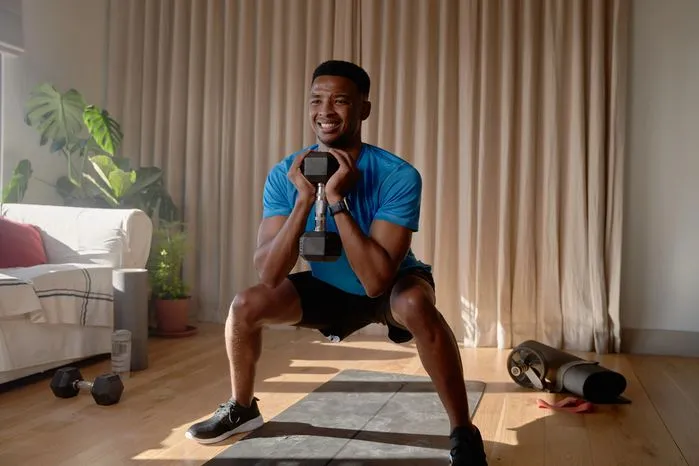 An image of a man doing goblet squats with a dumbbell at home—learn the key dimensions of physical health that build strength, energy, and wellness.