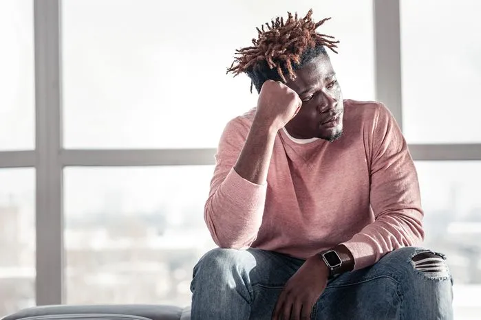 An image of a young man looking lost in thought near a window.