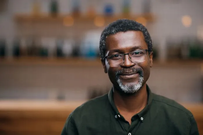 An image of a smiling middle-aged man in glasses and a green shirt in a warmly lit setting.