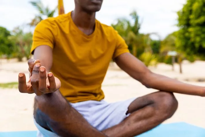 An image of a person sitting cross-legged outdoors in meditation with hands in a mudra gesture.