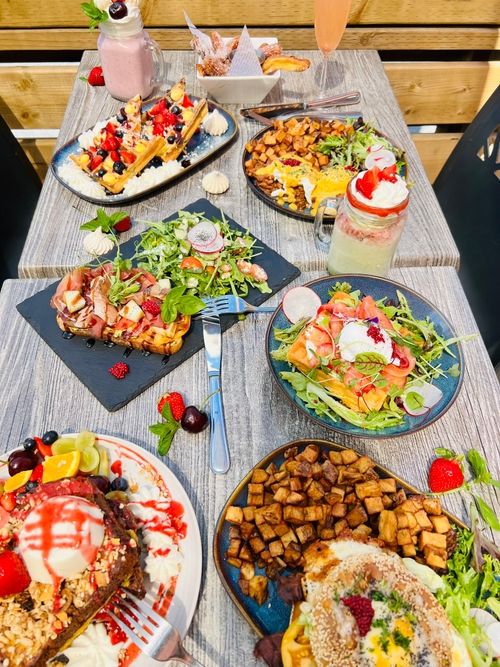 Table with breakfast dishes including waffles, eggs benedict, salad, potatoes, and fruit smoothies.