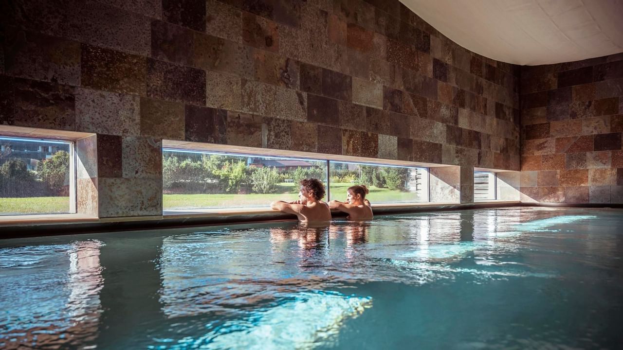 Casal na piscina indoor com vista para o jardim