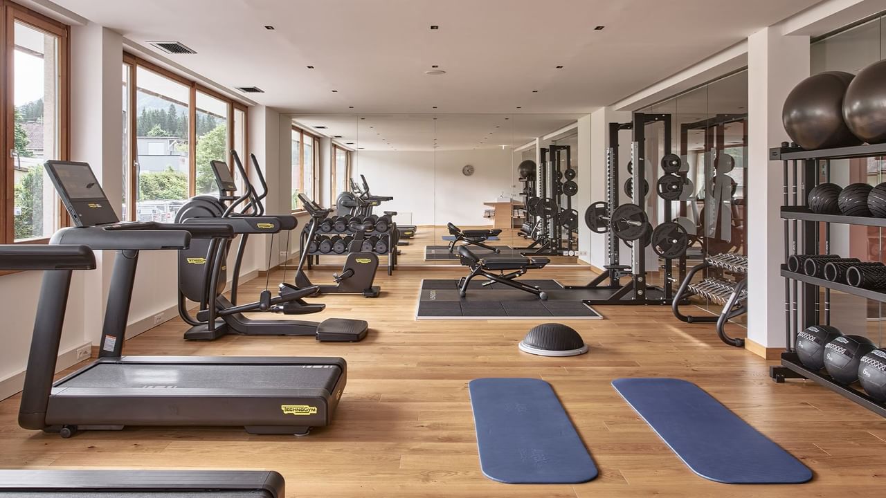 Academia com esteiras, pesos e equipamentos de musculação em piso de madeira