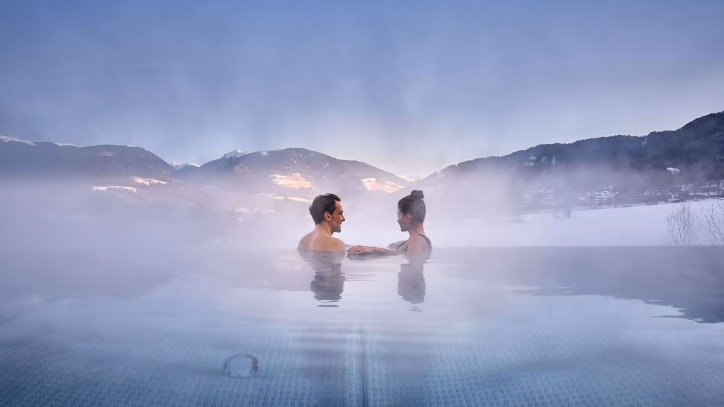 Casal relaxando em piscina com névoa e vista para as montanhas no inverno