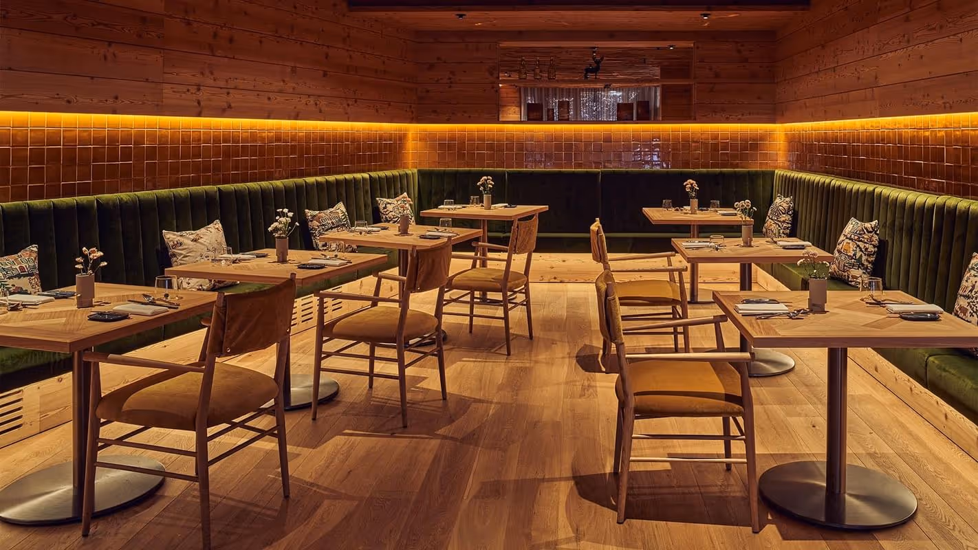 Restaurante elegante com mesas de madeira e iluminação aconchegante no Falkensteiner Hotel Kronplatz