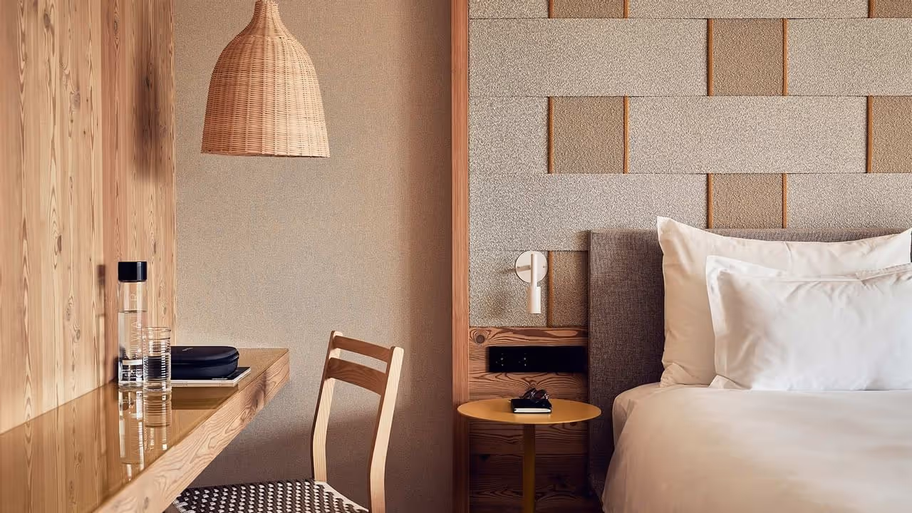 Quarto aconchegante com mesa de madeira, cadeira, cama e abajur trançado