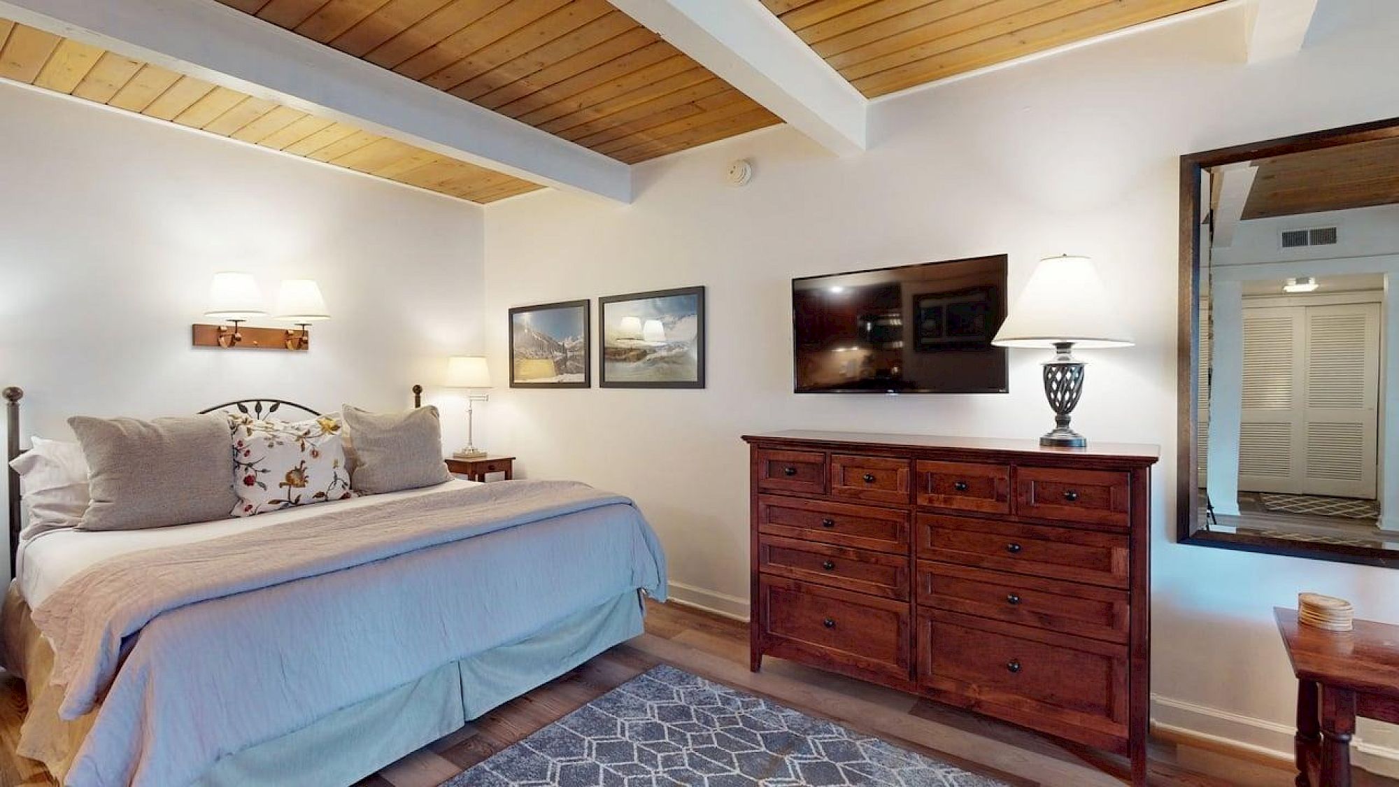 Quarto aconchegante com cama, móveis em madeira, TV e quadros decorativos