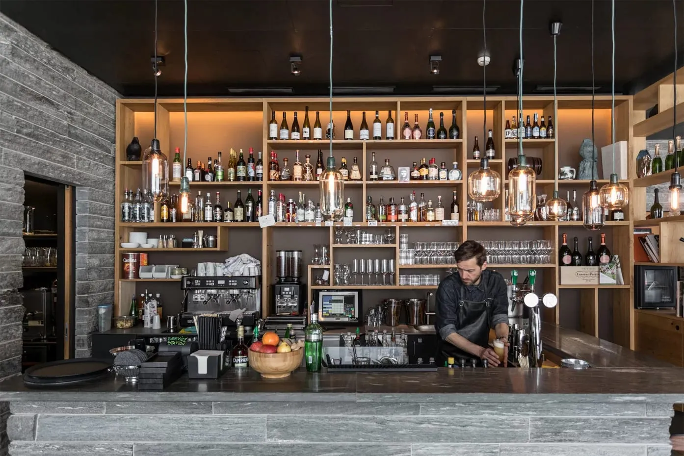 Bartender preparando drinque em bar com prateleiras de bebidas