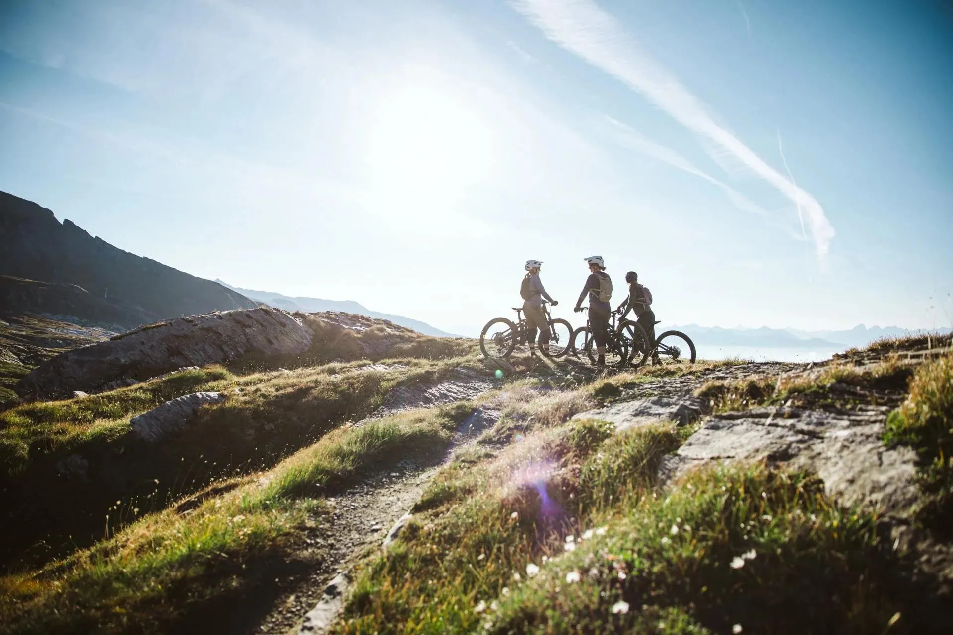 Três ciclistas de mountain bike em trilha alpina ensolarada