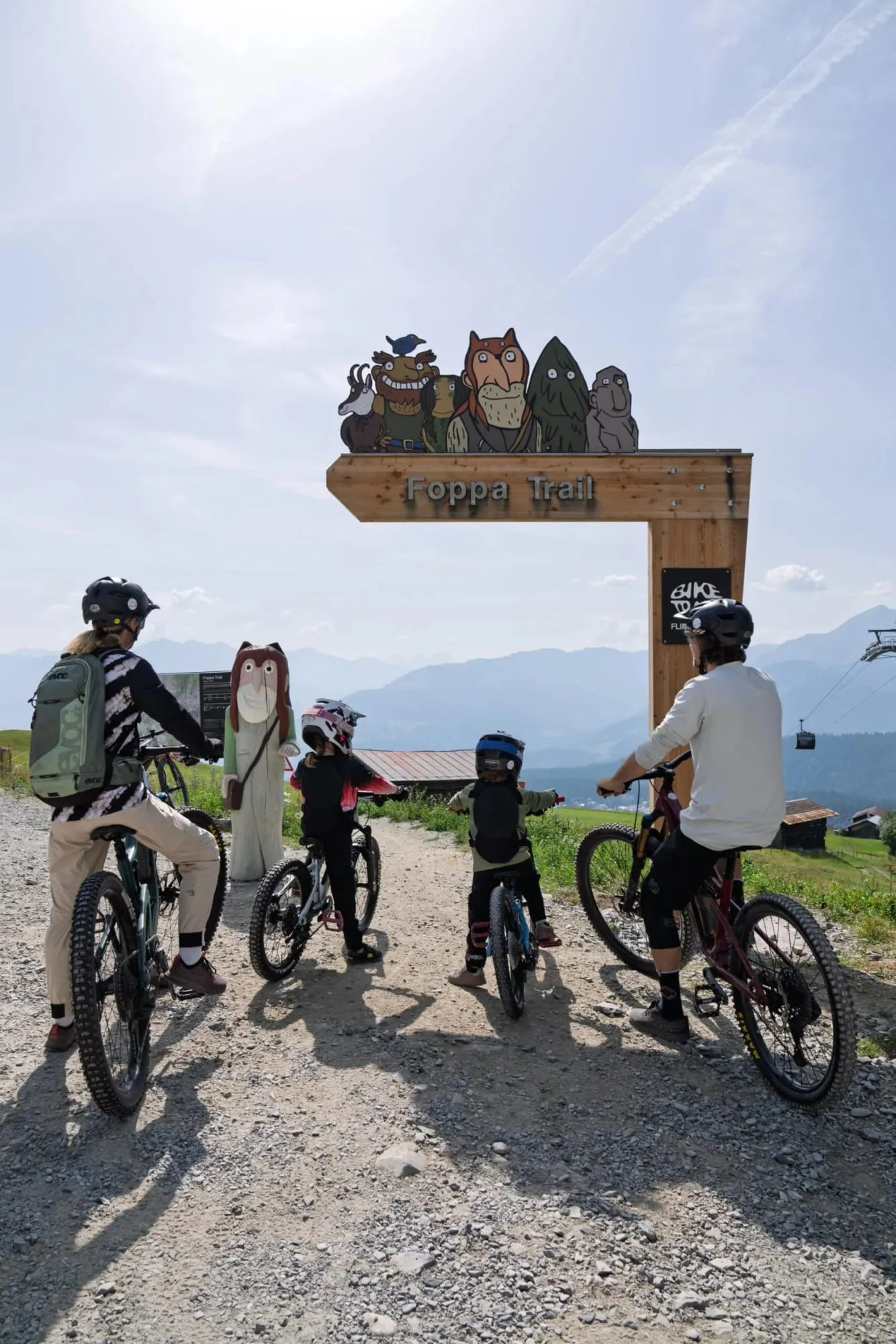 Família com bicicletas em trilha de montanha sob totem infantil