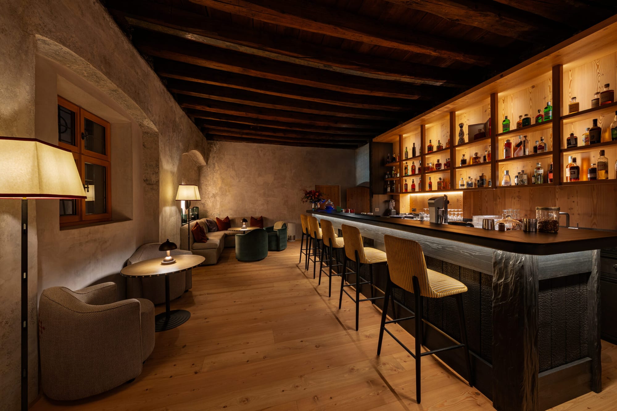Bar elegante com prateleiras iluminadas e banquetas altas em ambiente rústico