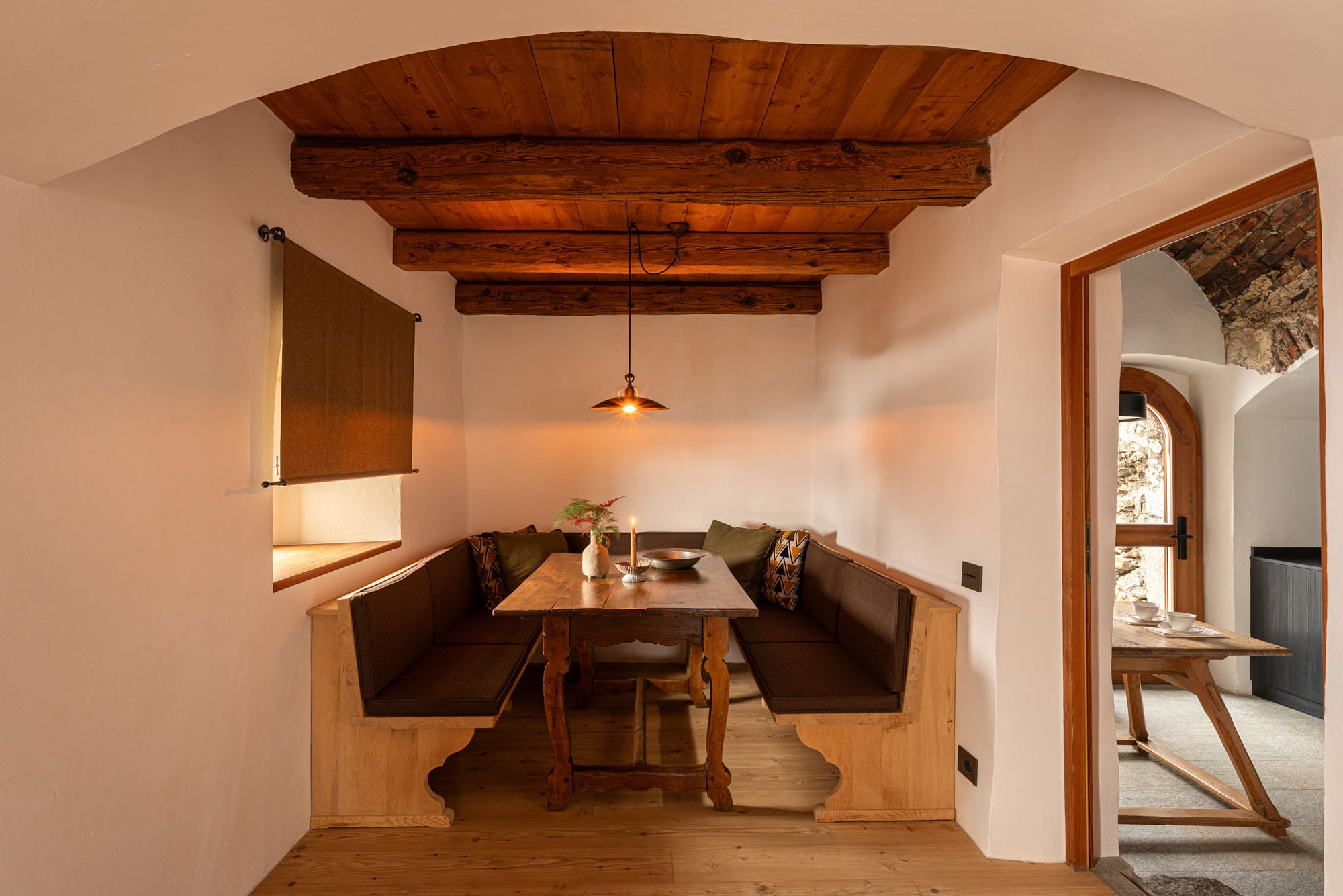 Cantinho de refeição com banco estofado e mesa de madeira sob arco