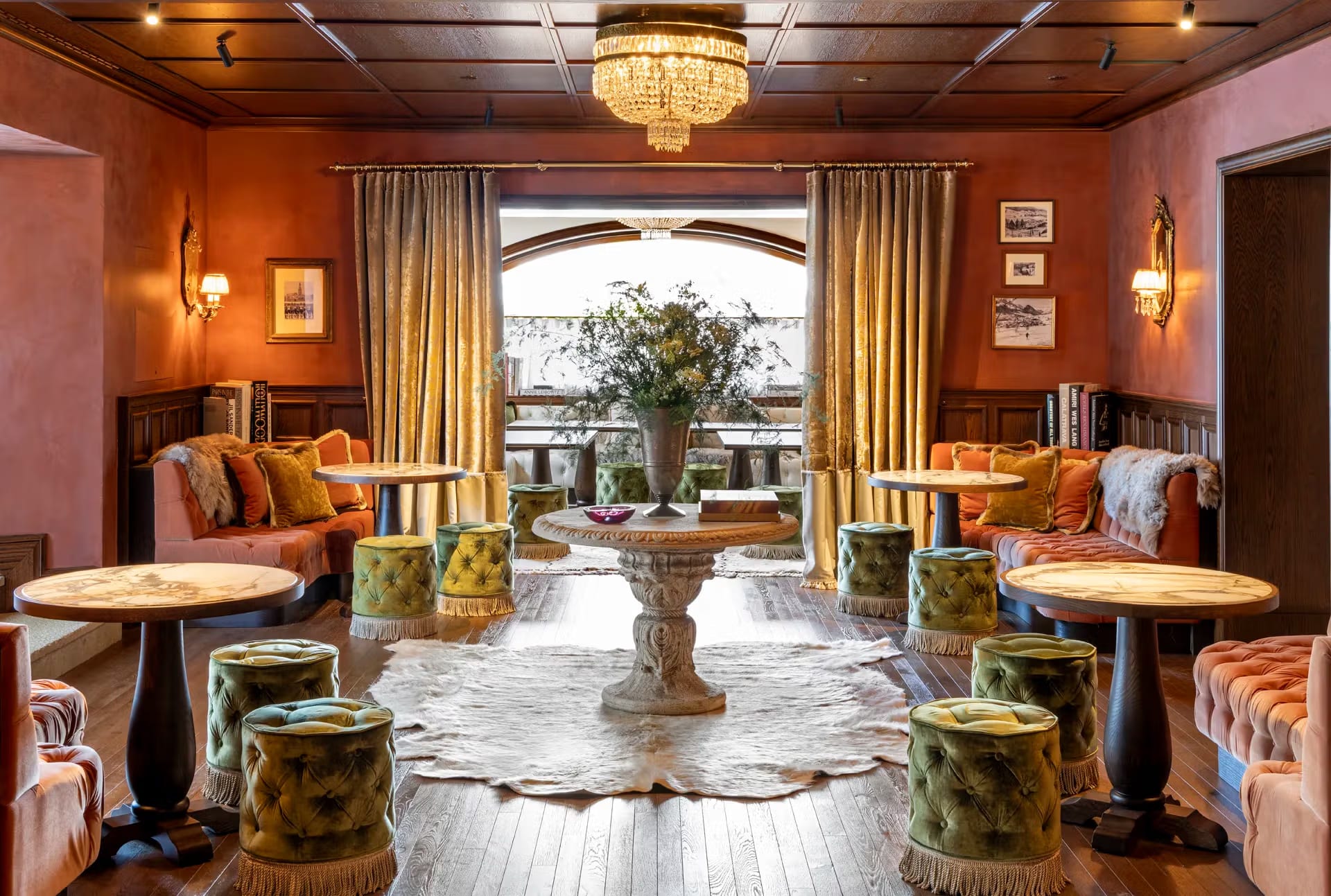 Lounge aconchegante com paredes terracota, banquetas verdes e lustre