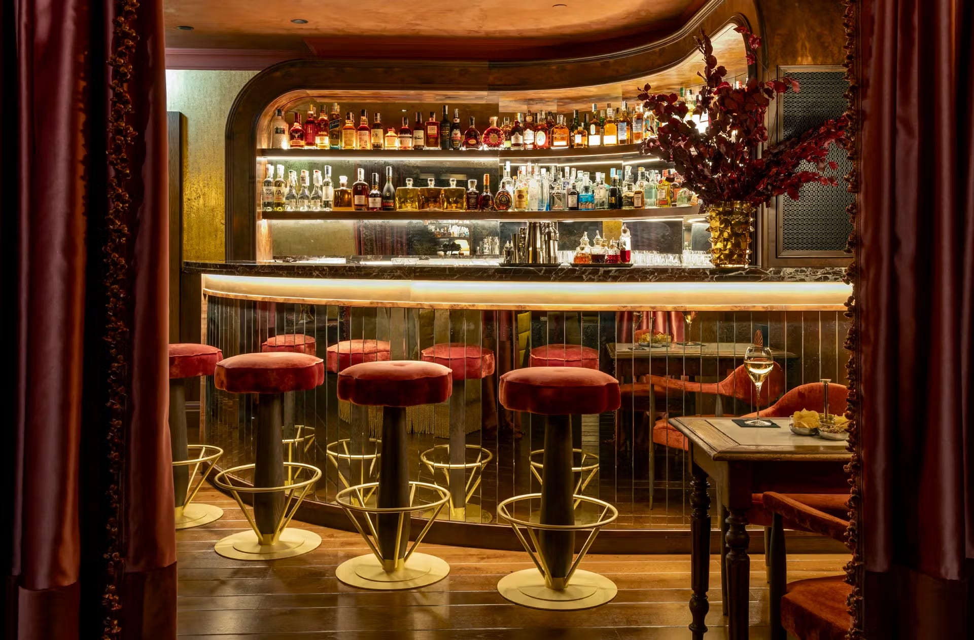 Bar sofisticado com banquetas de veludo vermelho e prateleiras iluminadas