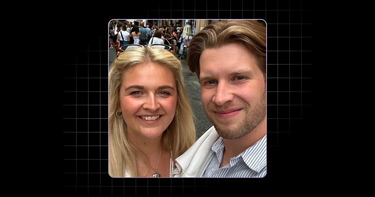 Smiling young man and woman taking a selfie on a busy street with people and shops behind them.