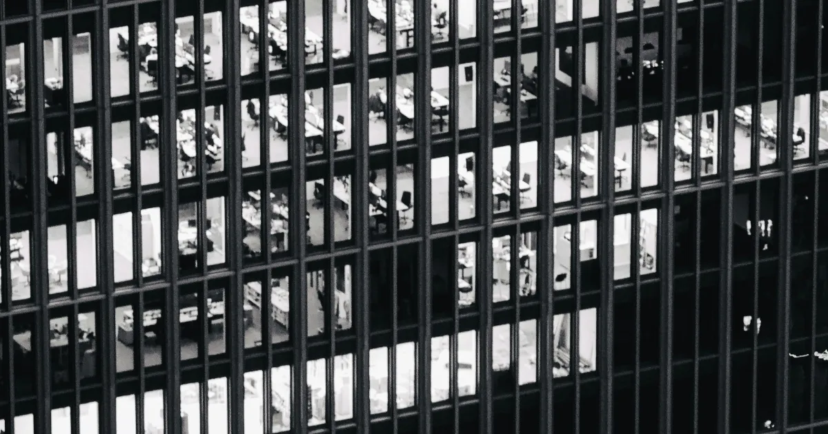 Black and white photo of office floors with desks and chairs seen through building windows.