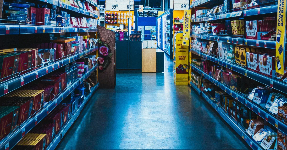 Supermarket aisle stocked with colourful consumer goods, stretching into the distance