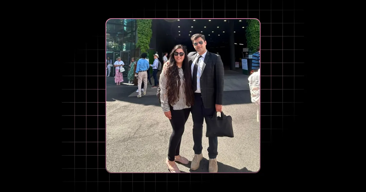 Man in suit and woman in striped shirt and leggings standing outdoors on sunny pavement.