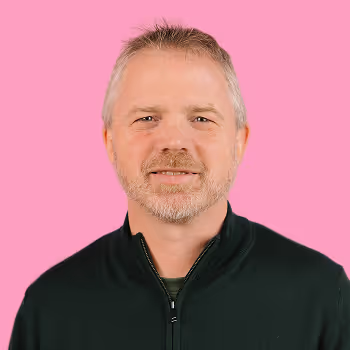 Portrait of Tristan, Senior Director of Risk & Compliance at Freetrade, on a pink background.