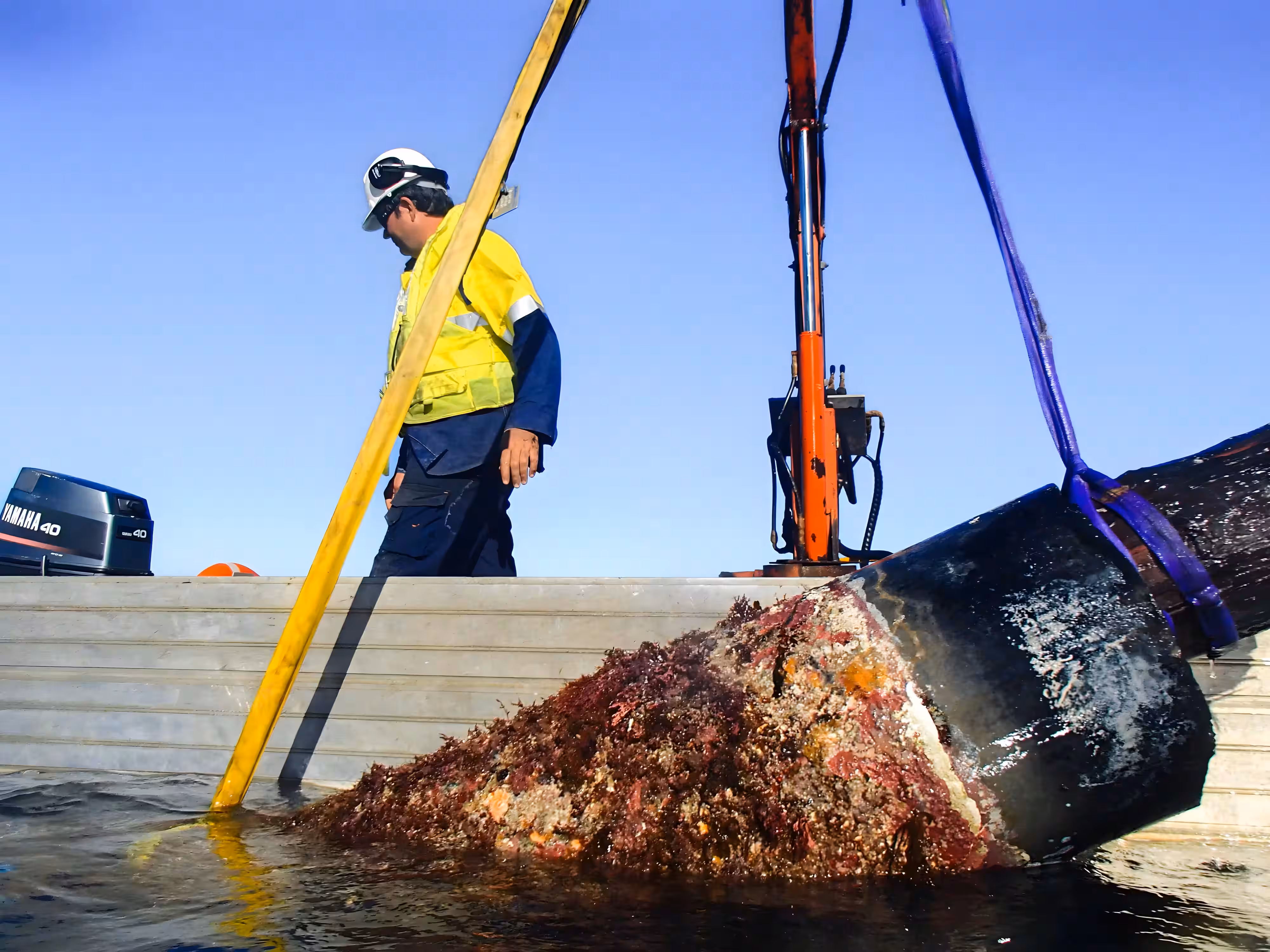 Worker on a vessel handling a heavily fouled marine pile using lifting equipment