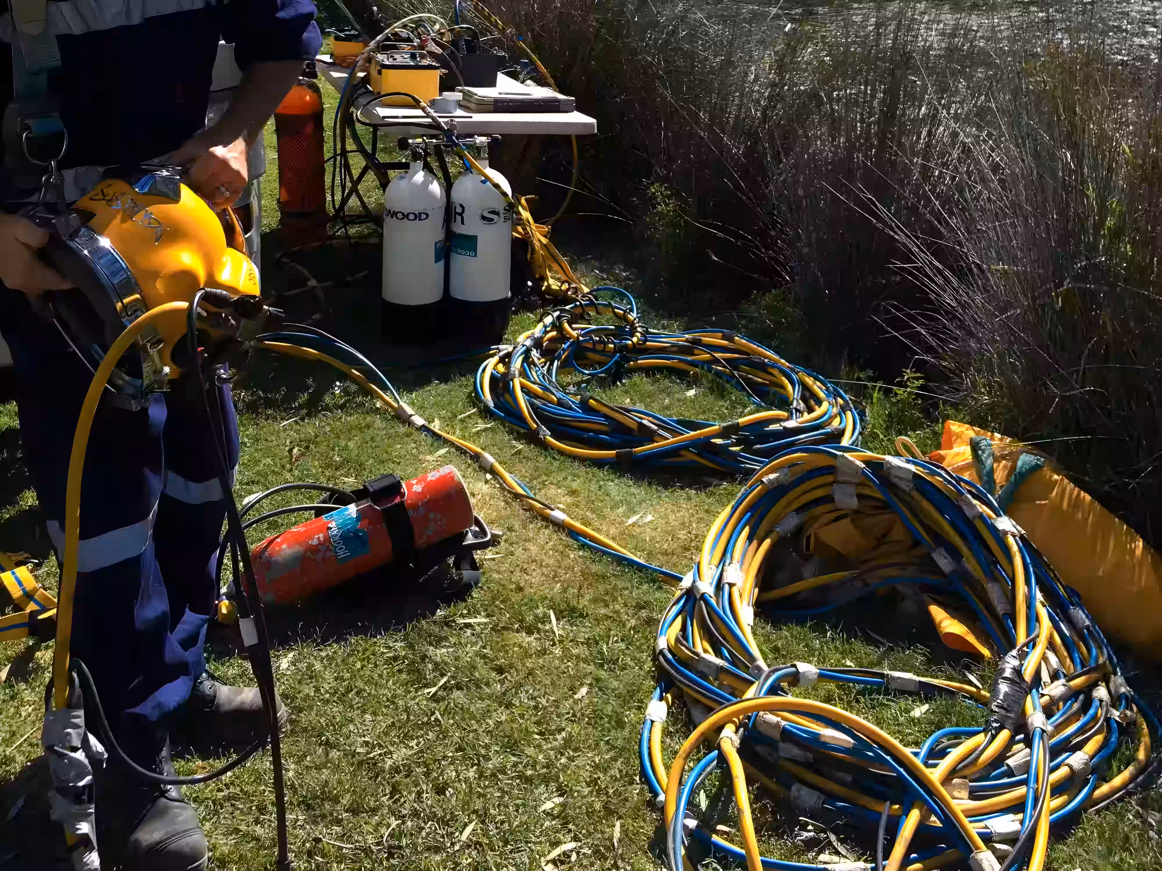 Surface-supplied diving setup with helmet, air cylinders, and umbilical hoses prepared for marine works