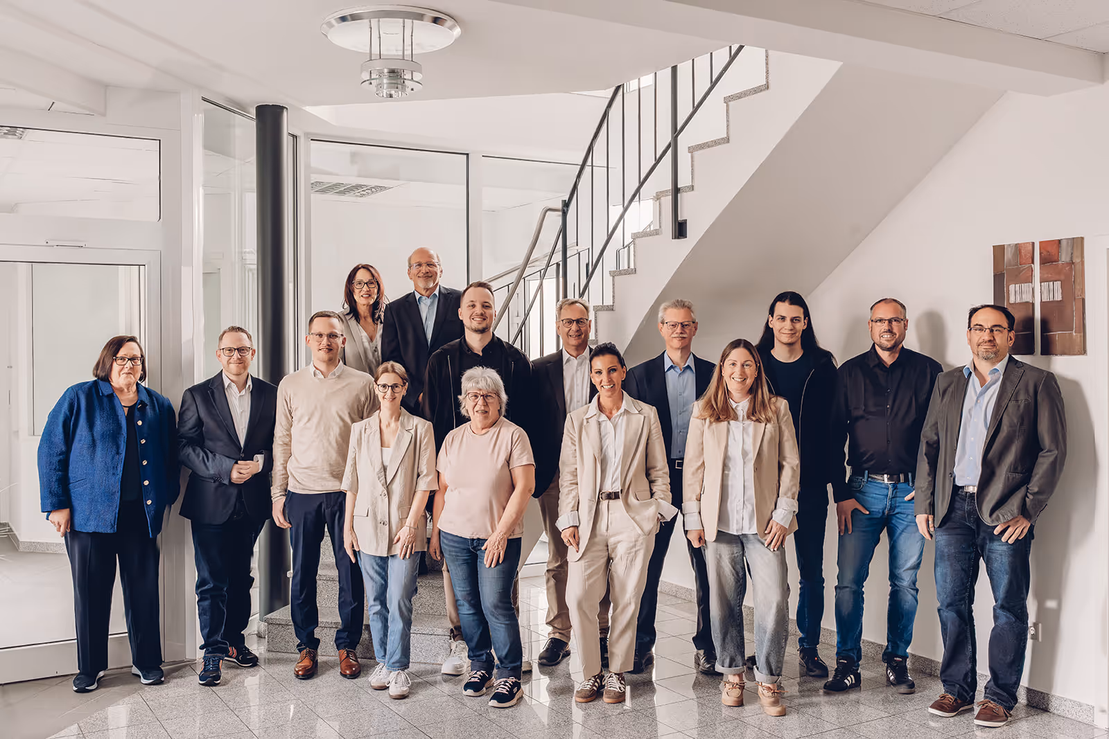 Gruppenfoto von 15 Personen, die in einem hellen Raum vor einer Treppe stehen