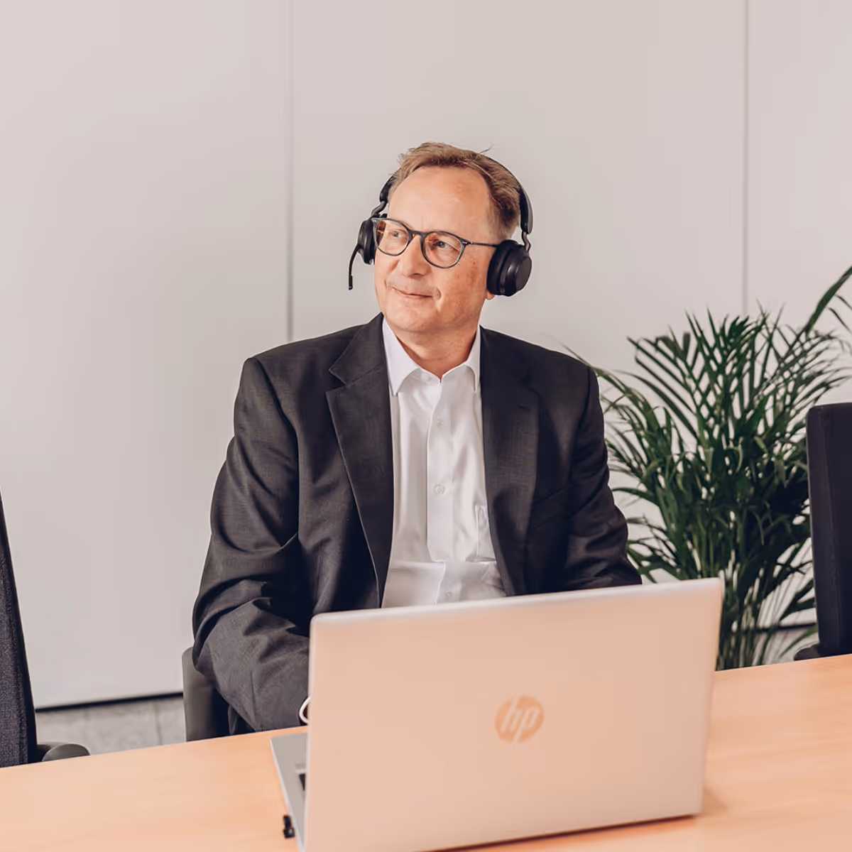Mann im Anzug mit Headset sitzt vor einem Laptop an einem Holztisch im Büro.
