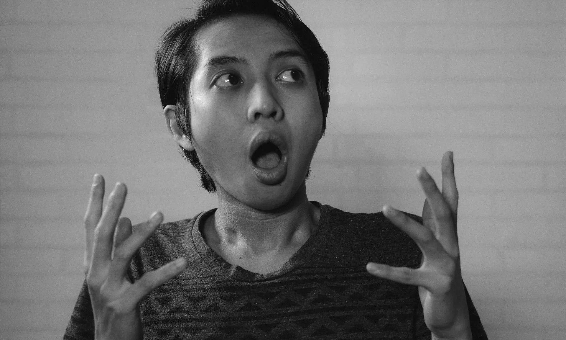 A person pulling an exaggerated shocked expression with hands raised, in black and white