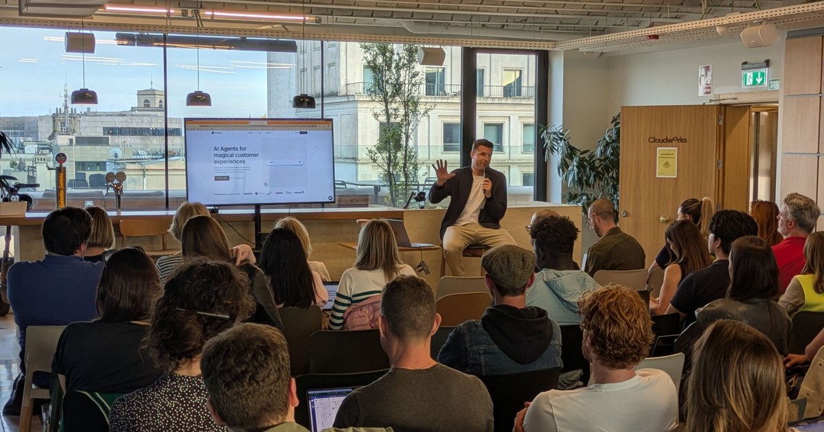 A Hello Operator AI workshop in progress: the speaker, holding a microphone, talks to attendees with laptops open, in front of a screen showing a slide about AI agents.