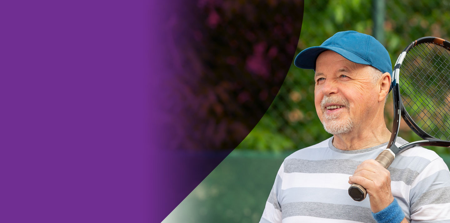 An older gentleman holding a tennis racket and wearing a blue cap.