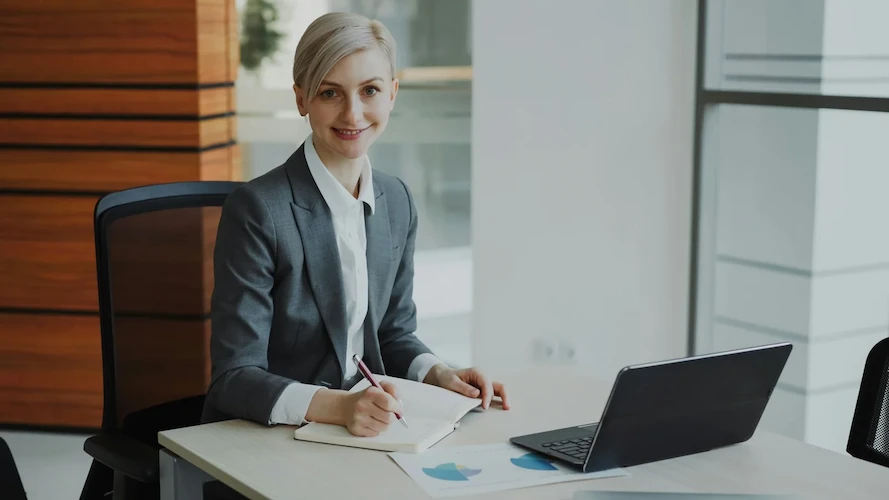 Femme professionnelle en costume au travail à son bureau, ordinateur portable ouvert, ambiance cabinet juridique.