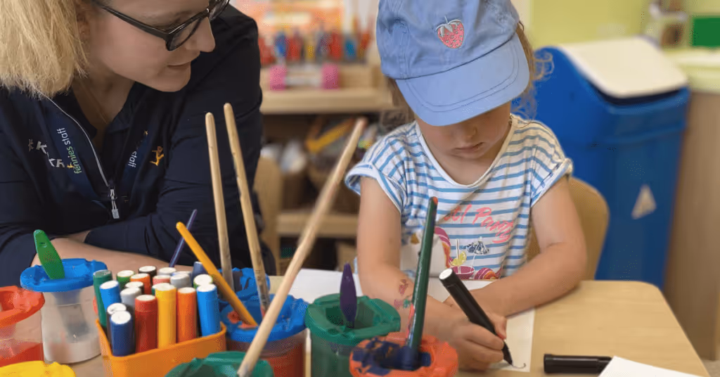 child painting in nursery with early years practitioner