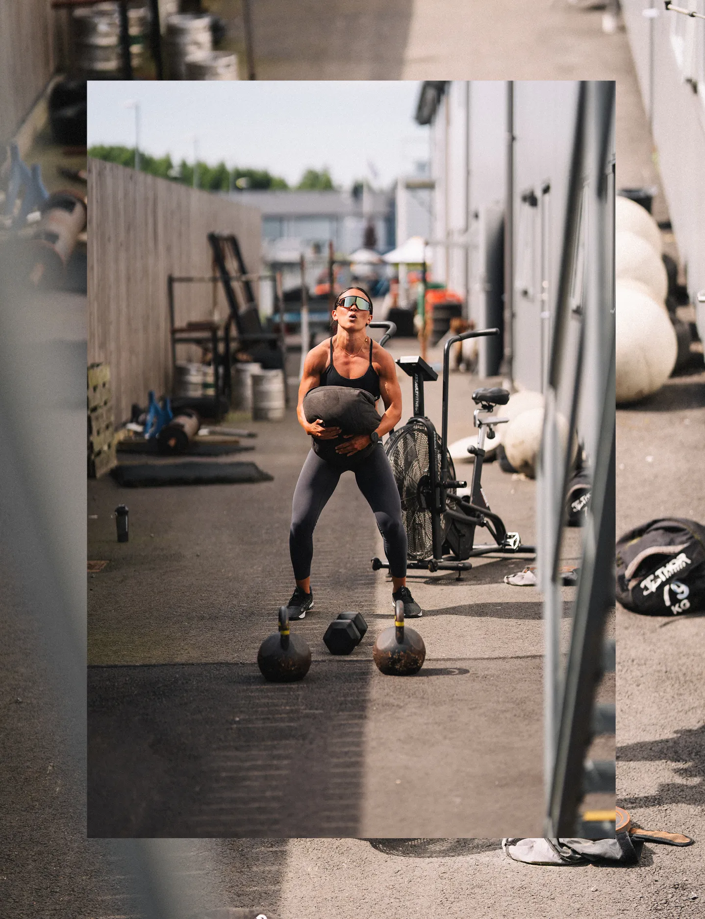 Muscular woman lifting a sandbag during an outdoor workout in an urban fitness area.