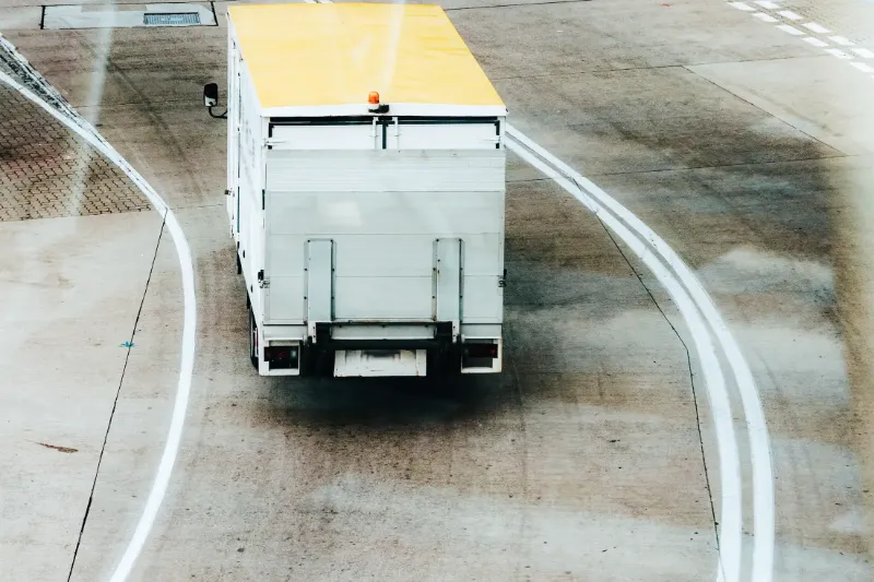 Service truck with yellow roof and warning light driving along curved pavement lines in an industrial area.