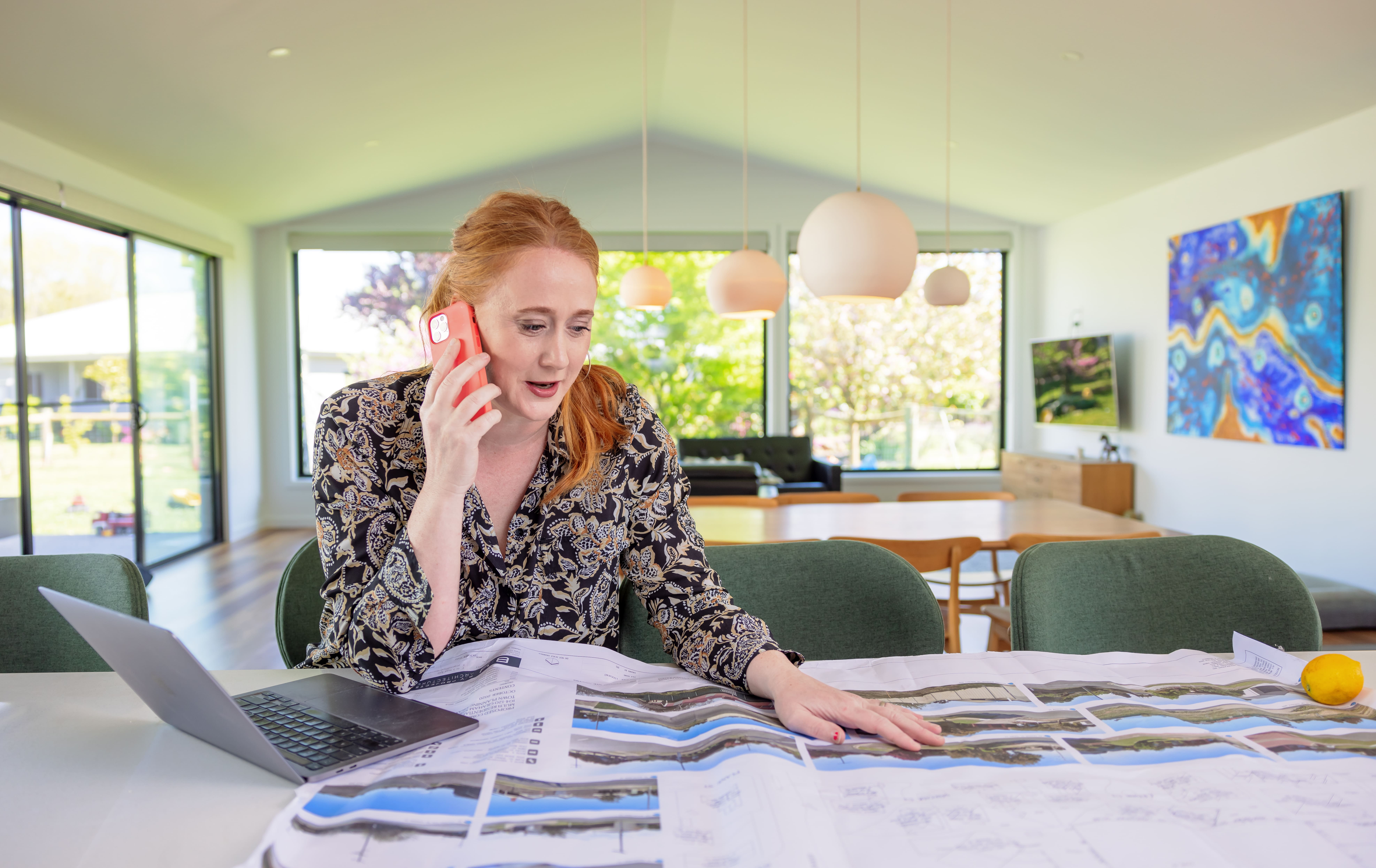 A woman working hard on the phone and looking at printed plans and on an open laptop.