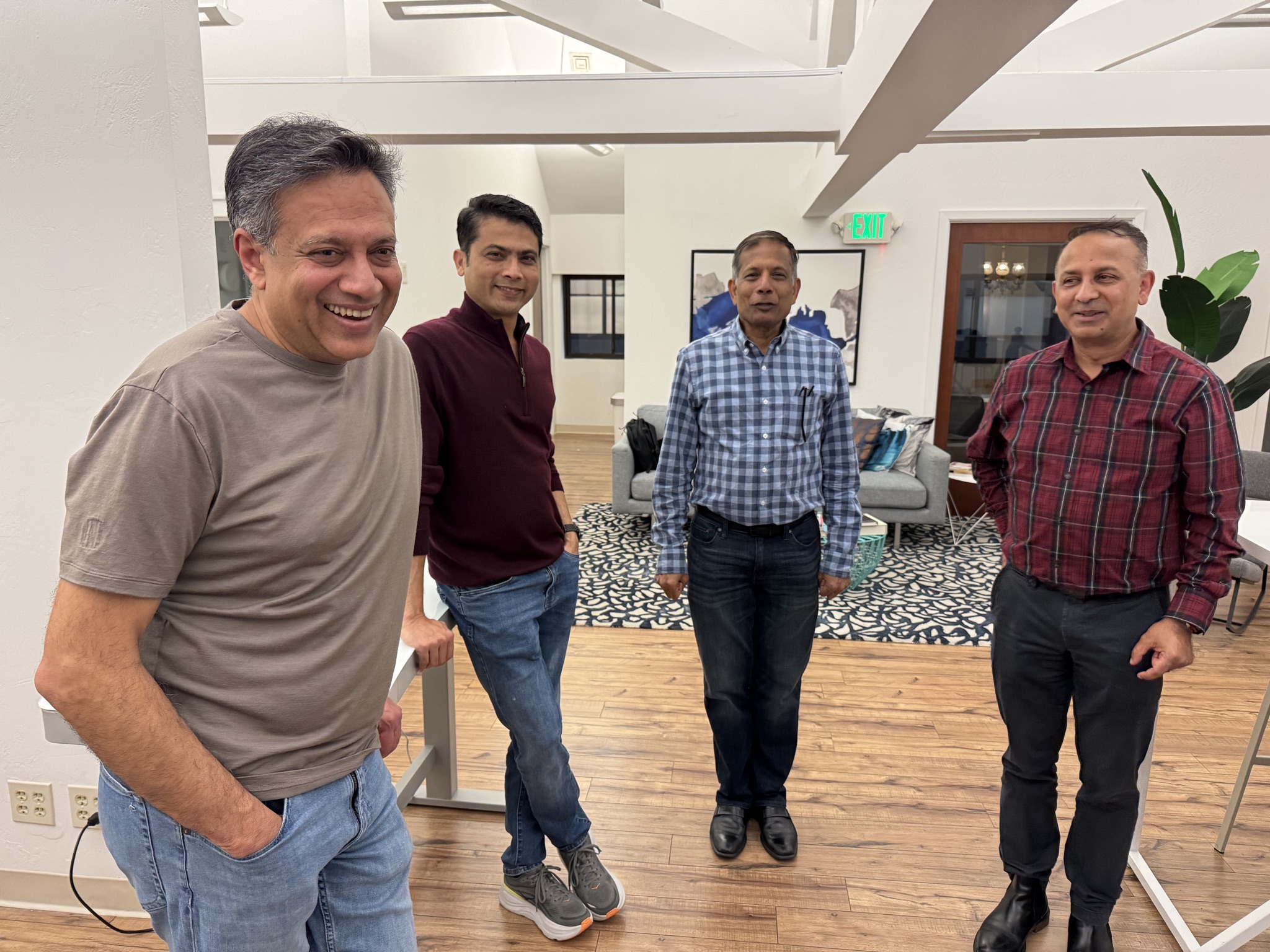 Four entrepreneurs stand in a well-lit indoor space, dressed in casual business attire, engaged in conversation.
