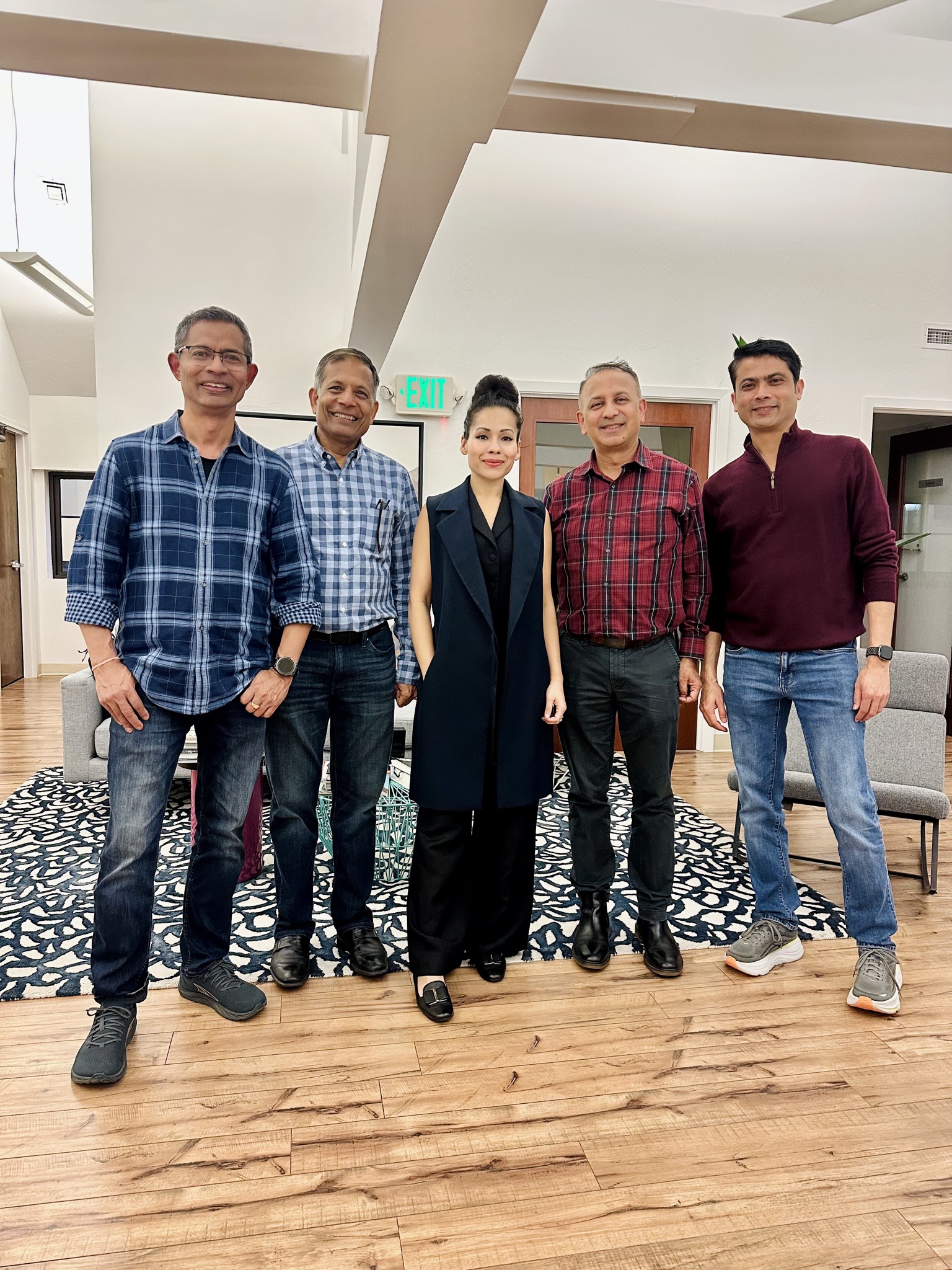 Five diverse entrepreneurs pose for a photo in a well-lit, modern office lobby with wood floors and abstract rug.