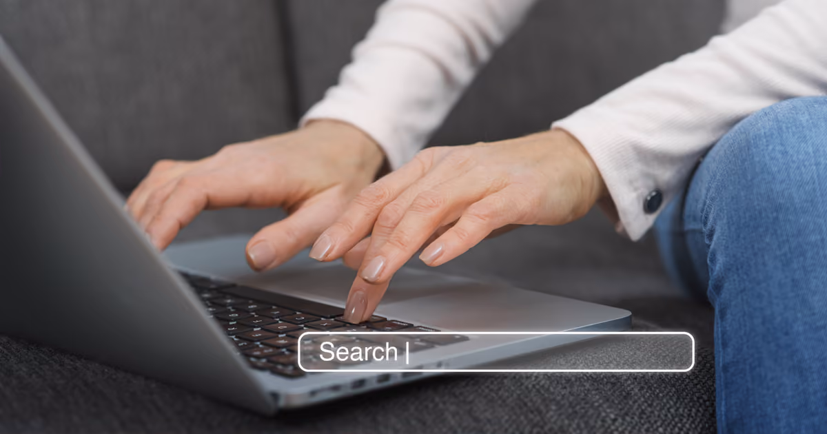 Close-up of hands typing on a laptop with an overlaid search bar, representing onsite search functionality on a website.