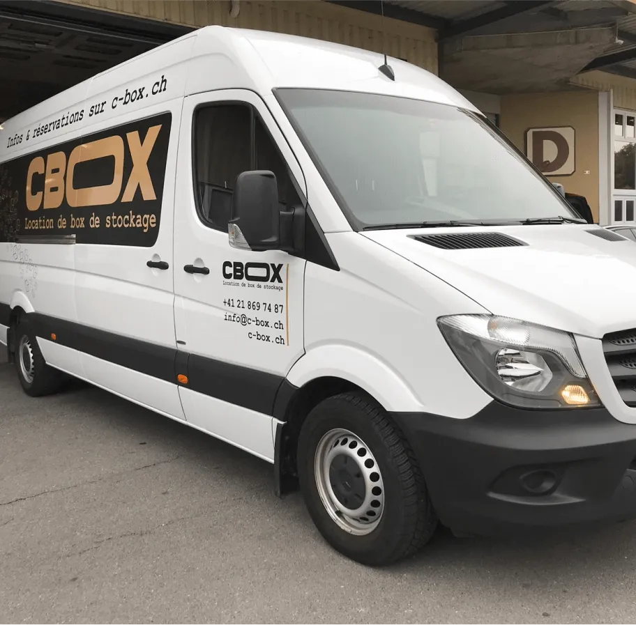 Camionnette de location C-BOX idéale pour les déménagements garée devant des portes de garage illustrées avec des indications de tailles de box de stockage et informations de contact.